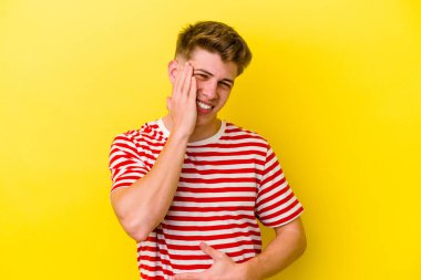 Sarı arka planda izole edilmiş genç beyaz adam mutlu bir şekilde gülüyor ve ellerini karnının üstünde tutarak eğleniyor..