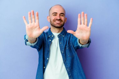 Mor arka planda izole edilmiş beyaz kel bir adam 10 numarayı elleriyle gösteriyor..