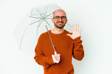 Şemsiyesini tutan genç kel adam gülümseyerek beş numarayı parmaklarıyla gösteriyor..