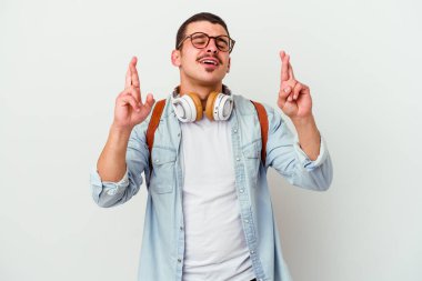 Beyaz arka planda izole edilmiş müzik dinleyen beyaz tenli genç bir öğrenci şans getirsin diye dua ediyor.