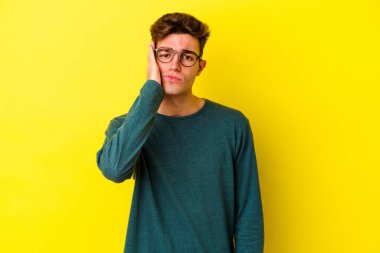 Sarı arka planda izole edilmiş genç beyaz adam yorgun ve uykulu bir şekilde ellerini başının üstünde tutuyor..