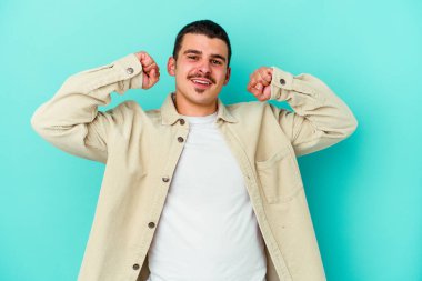 Mavi arka planda izole genç beyaz adam özel bir günü kutluyor, atlıyor ve enerjiyle kollarını kaldırıyor..