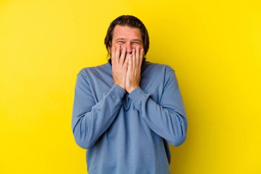 Orta yaşlı beyaz bir adam sarı arka planda izole edilmiş bir şekilde bir şeye gülüyor, ağzı ellerle örtüyor..