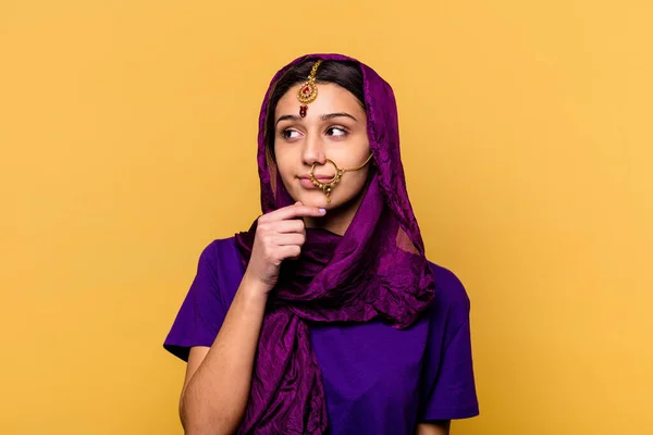 若いですインドの女性を身に着けています伝統的なサリーの服は疑わしいと懐疑的な表現と横に見える黄色の背景に隔離 — ストック写真