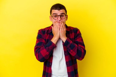 Sarı arka planda izole edilmiş, ağzı ellerle kaplanmış, yeni bir şey keşfetmeye hevesli genç beyaz bir adam..