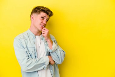 Sarı arka planda izole edilmiş genç beyaz adam rahatlamış bir şeyin fotokopi odasına baktığını düşünüyor..