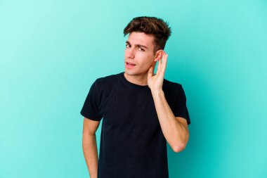 Mavi arka planda izole edilmiş genç beyaz adam bir dedikoduyu dinlemeye çalışıyor..