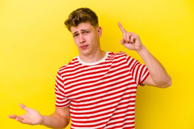 Genç beyaz adam sarı arka planda izole edilmiş ve elinde bir ürün var..