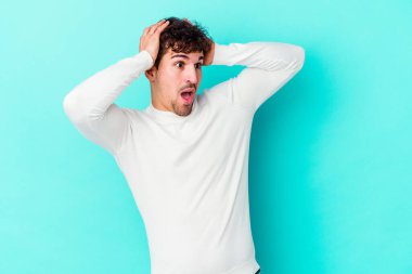 Genç beyaz adam mavi arka planda izole edilmiş bağırıyor, çok heyecanlı, tutkulu, bir şeyden memnun..