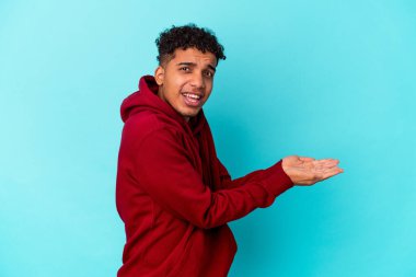 Genç Afro-Amerikalı kıvırcık adam mavi üzerine izole edilmiş. Elinde palmiye üzerinde bir kopya alanı var..