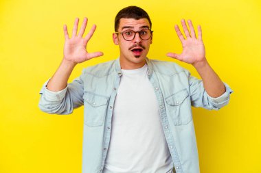 Sarı arka planda izole edilmiş genç beyaz adam gökyüzüne haykırıyor, yukarı bakıyor, hayal kırıklığına uğramış..