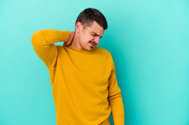 Kafkasyalı genç adam mavi arka planda izole edilmiş. Stres yüzünden boynu ağrıyor. Masaj yapıyor ve elle dokunuyor..