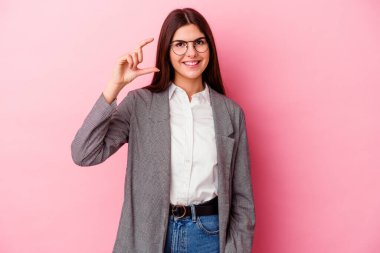 Kafkasyalı genç bir iş kadını pembe arka planda izole edilmiş, parmakları olan, gülümseyen ve kendinden emin bir şey tutuyor..