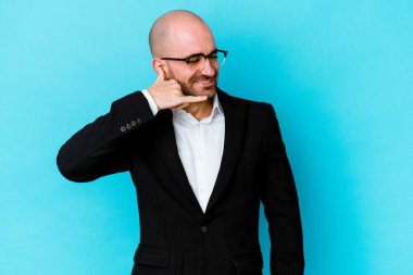 Genç, beyaz, kel bir adam mavi arka planda izole edilmiş. Cep telefonu hareketini parmaklarıyla gösteriyor..