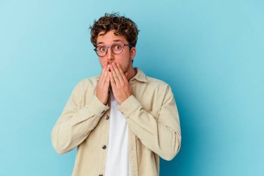 Mavi arka planda gözlüklü genç beyaz adam elleri ile ağzını kapatırken şok oldu..