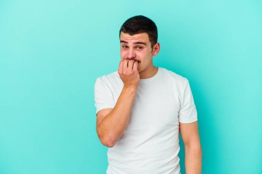 Mavi arka planda izole edilmiş, tırnak yiyen, gergin ve endişeli genç bir beyaz adam..