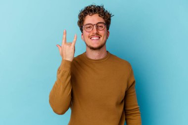 Mavi arka planda izole edilmiş gözlüklü genç beyaz adam parmaklarıyla taş hareketi gösteriyor.