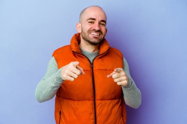 Kafkasyalı kel adam, mor arka planda izole edilmiş, gülümseyen, ön tarafı işaret eden..