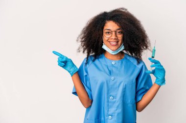 Genç Afro-Amerikan kıvırcık saçlı kadın elinde şırıngayla gülümsüyor ve boş alana bir şey gösteriyor..