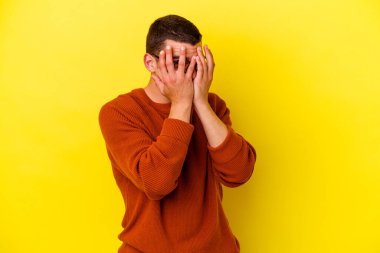 Sarı arka planda izole edilmiş beyaz, genç bir adam kameraya parmaklarıyla göz kırpıyor, yüzünü kapatmaktan utanıyor..