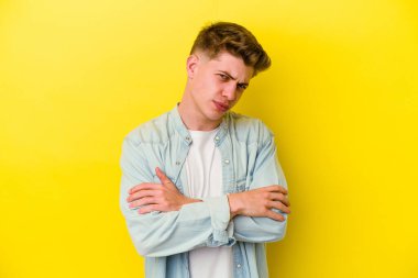 Sarı arka planda izole edilmiş genç beyaz adam hoşnutsuzca kaşlarını çatmış, kollarını kavuşturmuş..