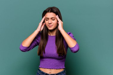 Genç Hintli kadın mavi arka planda izole edilmiş tapınaklara dokunuyor ve baş ağrısı çekiyor..