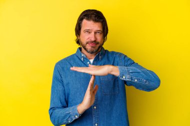 Orta yaşlı beyaz bir adam sarı arka planda izole edilmiş bir şekilde mola veriyor..