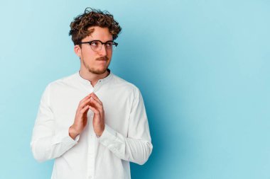 Kafkasyalı genç bir iş adamı mavi arka planda izole edilmiş bir plan kuruyor, bir fikir kuruyor..