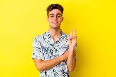Sarı arka planda izole edilmiş genç beyaz adam iki numarayı parmaklarıyla gösteriyor..