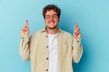 Gözlüklü genç beyaz adam mavi arka planda izole edilmiş şans dilemek için şans diliyor.