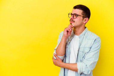 Sarı arka planda izole edilmiş, şüpheli ve şüpheci bir ifadeyle yan bakan genç beyaz adam..