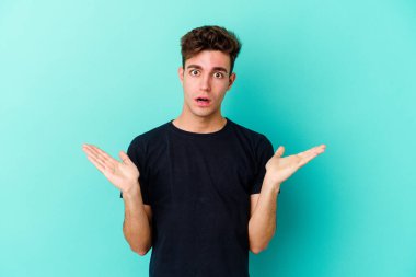 Kafkasyalı genç adam mavi arka planda izole edildi. Şaşırdı ve şok oldu..