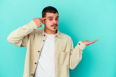 Kafkasyalı genç adam mavi arka planda izole edilmiş ve elinde bir ürün tutuyor..