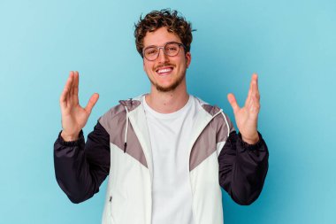 Mavi arka planda gözlüklü genç beyaz adam hoş bir sürpriz alıyor, heyecanlı ve el kaldırıyor..