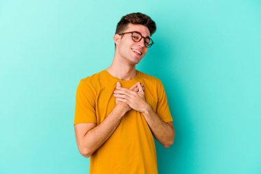 Mavi arka planda izole edilmiş beyaz bir genç, dost bir ifadeye sahip, avuçlarını göğsüne bastırıyor. Aşk konsepti.