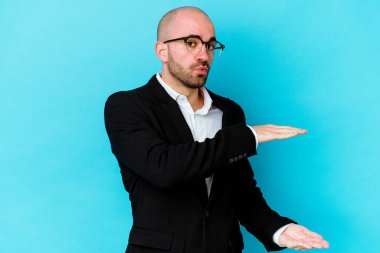 Mavi arka planda izole genç beyaz adam iki eliyle bir şey tutuyor, ürün sunumu.