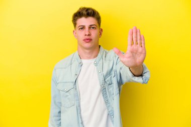 Sarı arka planda izole edilmiş genç beyaz adam elini uzatmış, dur işareti göstererek seni engelliyor..