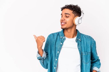 Genç Afro-Amerikalı kıvırcık adam kulaklıkla müzik dinliyor başparmağıyla işaret ediyor, gülüyor ve kaygısız..