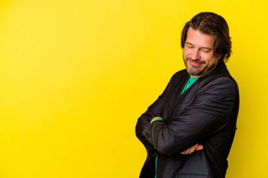 Sarı arka planda izole edilmiş orta yaşlı beyaz adam kollarını kavuşturarak gülümsüyor..