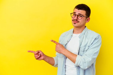 Sarı arka planda izole edilmiş genç beyaz adam işaret parmağıyla fotokopi alanını işaret ederek şok oldu..