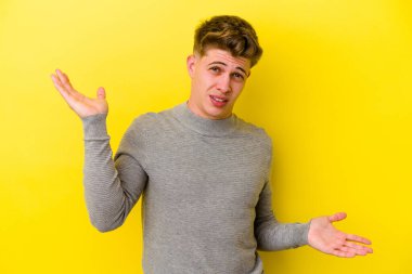 Kafkasyalı genç adam sarı arka planda izole edilmiş. Kafası karışmış ve omuz silkiyor. Kopya alanını tutmak için..