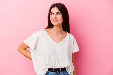 Pembe arka planda izole edilmiş genç beyaz kadın hedeflere ve amaçlara ulaşma hayali kuruyor.