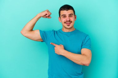 Mavi arka planda izole edilmiş genç beyaz adam güçlü bir hareket sergiliyor kollarıyla, kadınsı gücün sembolü.