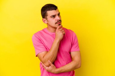 Kafkas asıllı genç adam sarı arka planda izole edilmiş düşünüyor ve yukarı bakıyor, yansıtıyor, düşünüyor, hayal kuruyor..