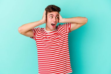 Genç beyaz adam mavi arka planda izole edilmiş bağırıyor, çok heyecanlı, tutkulu, bir şeyden memnun..