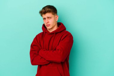 Kafkasyalı genç adam mavi arka planda izole edilmiş şüpheli, belirsiz, seni muayene ediyor..