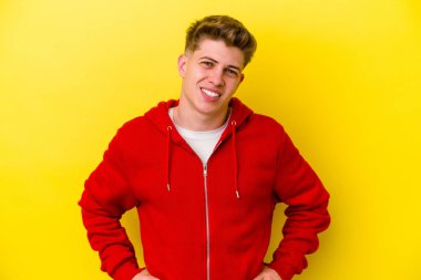 Sarı arka planda izole edilmiş genç beyaz adam ellerini kalçalarına koyuyor..