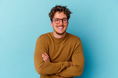 Mavi arka planda izole edilmiş gözlük takan genç beyaz adam gülüyor ve eğleniyor..