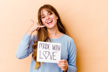 Elinde aşk levhasıyla gezen beyaz bir kadın, cep telefonu hareketini parmaklarıyla gösteriyor..