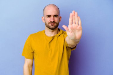Kafkasyalı genç kel adam mor arka planda izole edilmiş elini uzatmış, dur işareti gösteriyor, bu da seni engelliyor..